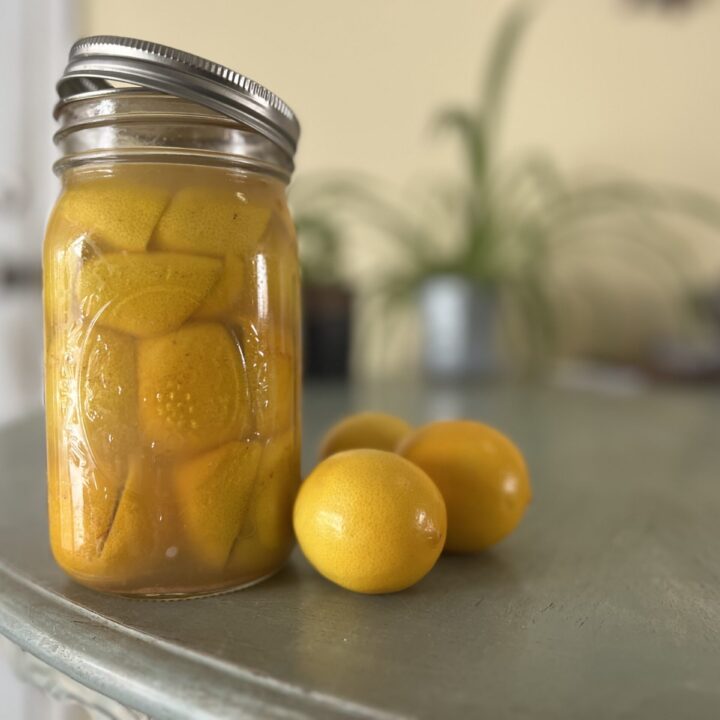 Mason jar on table with pickled lemons and fresh lemons.