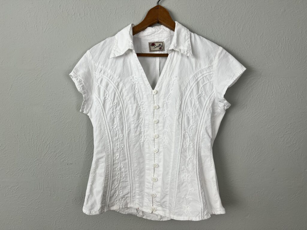 A white women's western shirt hanging on wall.
