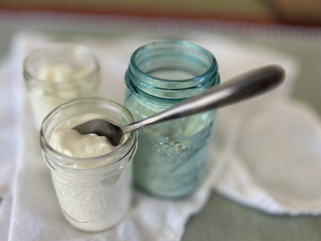 Three mason jars, 1 vintage blue one, with skyr yogurt in them and a spoon sticking out.
