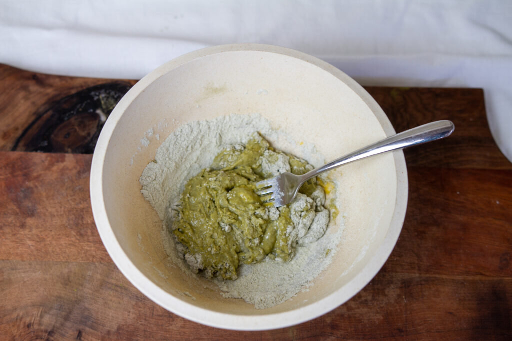 Mixing bowl with flour, nettles,and egg being mixed with a fork.