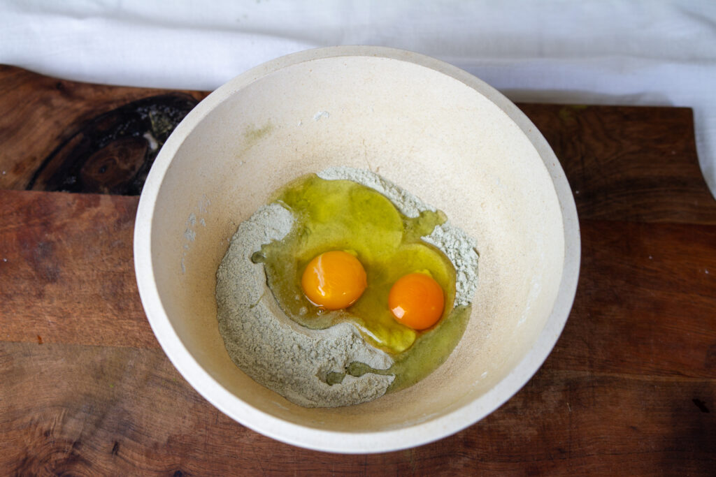 A mixing bowl with flour, nettles powder, and two eggs.