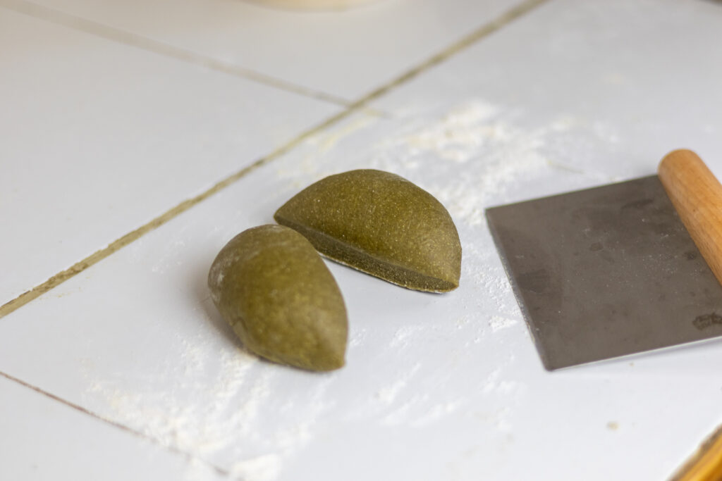 Pasta dough cut in two by a bench scraper next to it.