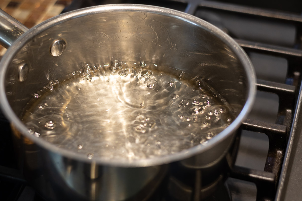 A silver pot on stove top with boiling simple syrup.