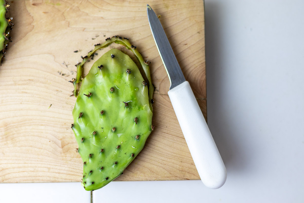 A fresh prickly pear pad on cutting board demonstrating how to remove the top part.