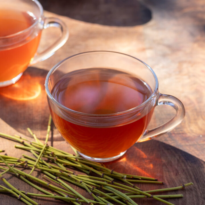 Brewed mormon tea behind ephedra stems on wooden table.