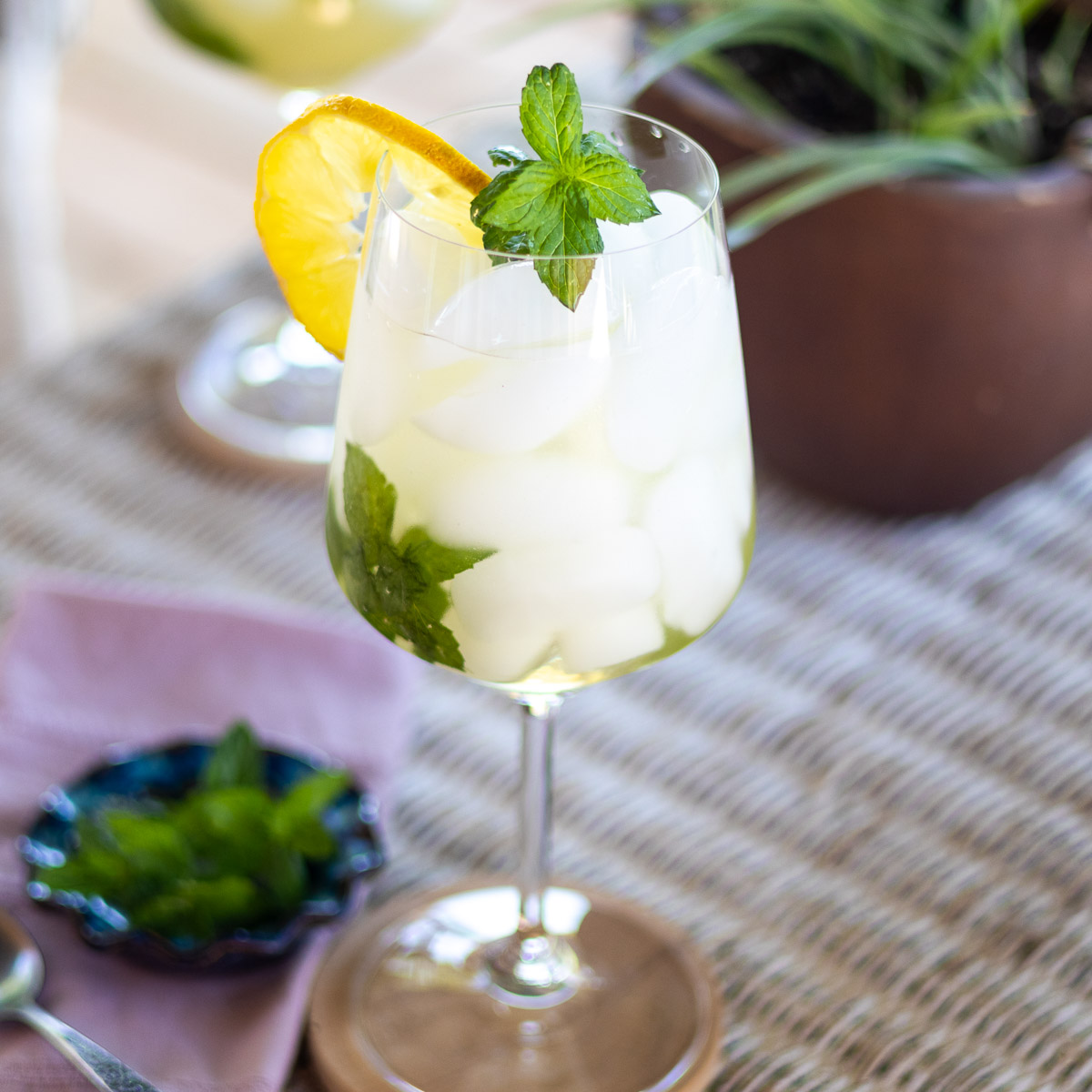An outdoor wicker table with a close up of the mint garnish on a Hugo Spritz cocktail.
