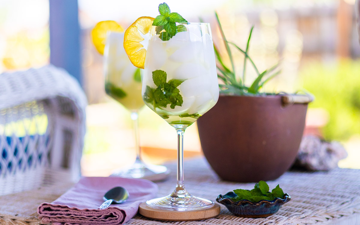 A Hugo cocktail on a patio with pink napkin, spoon, and dish of mint.
