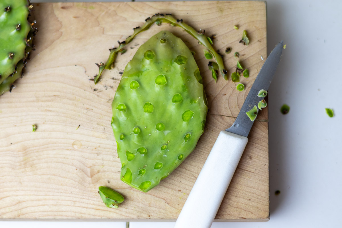 A fresh nopal on wood cutting board demonstrating the removal of areolas.