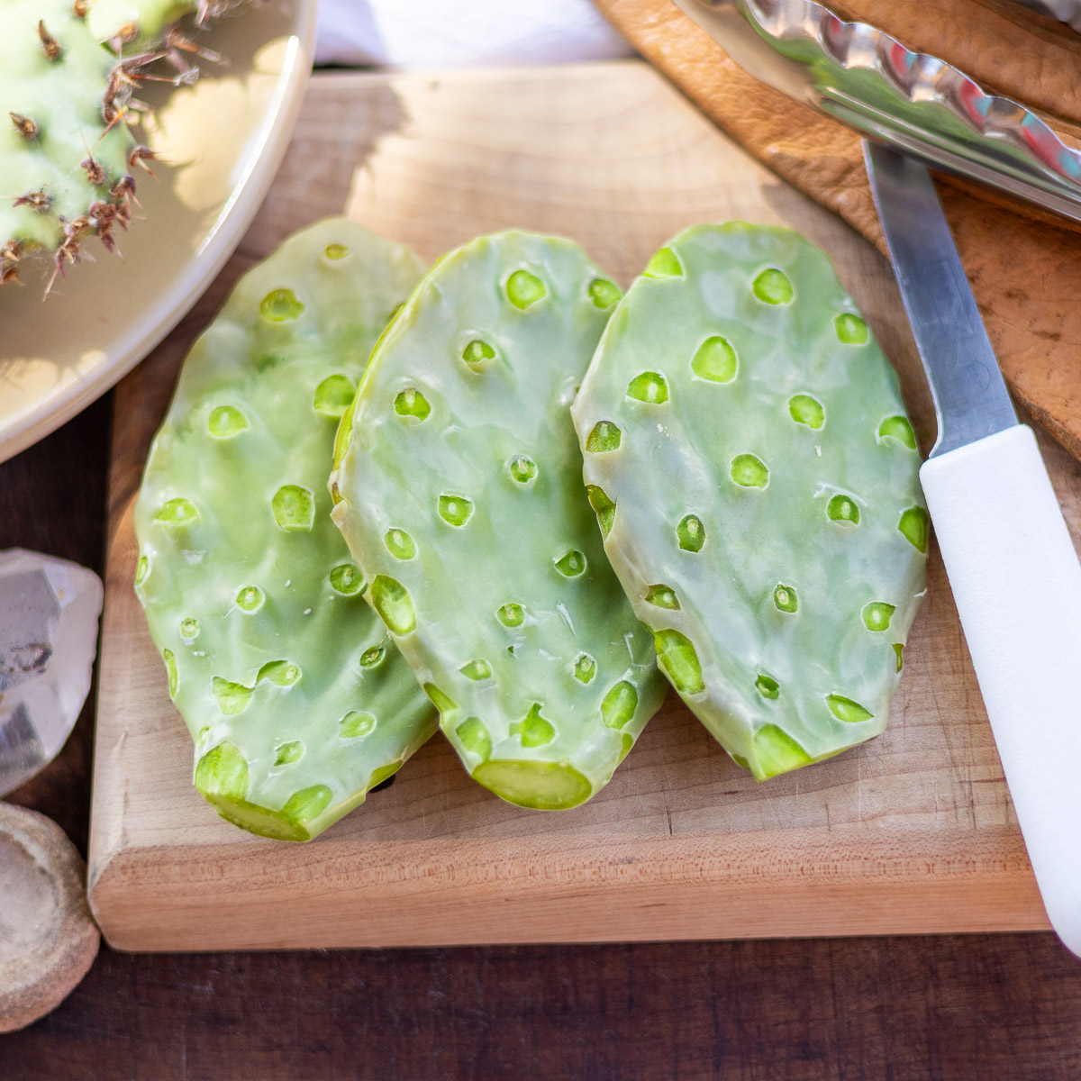 Three cleaned nopales on wood board next to tools.