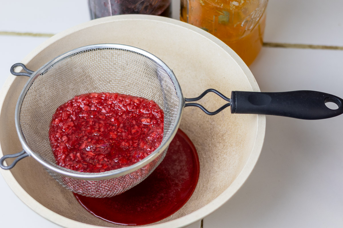 Strawberry syrup being strained from solids with mesh strainer.