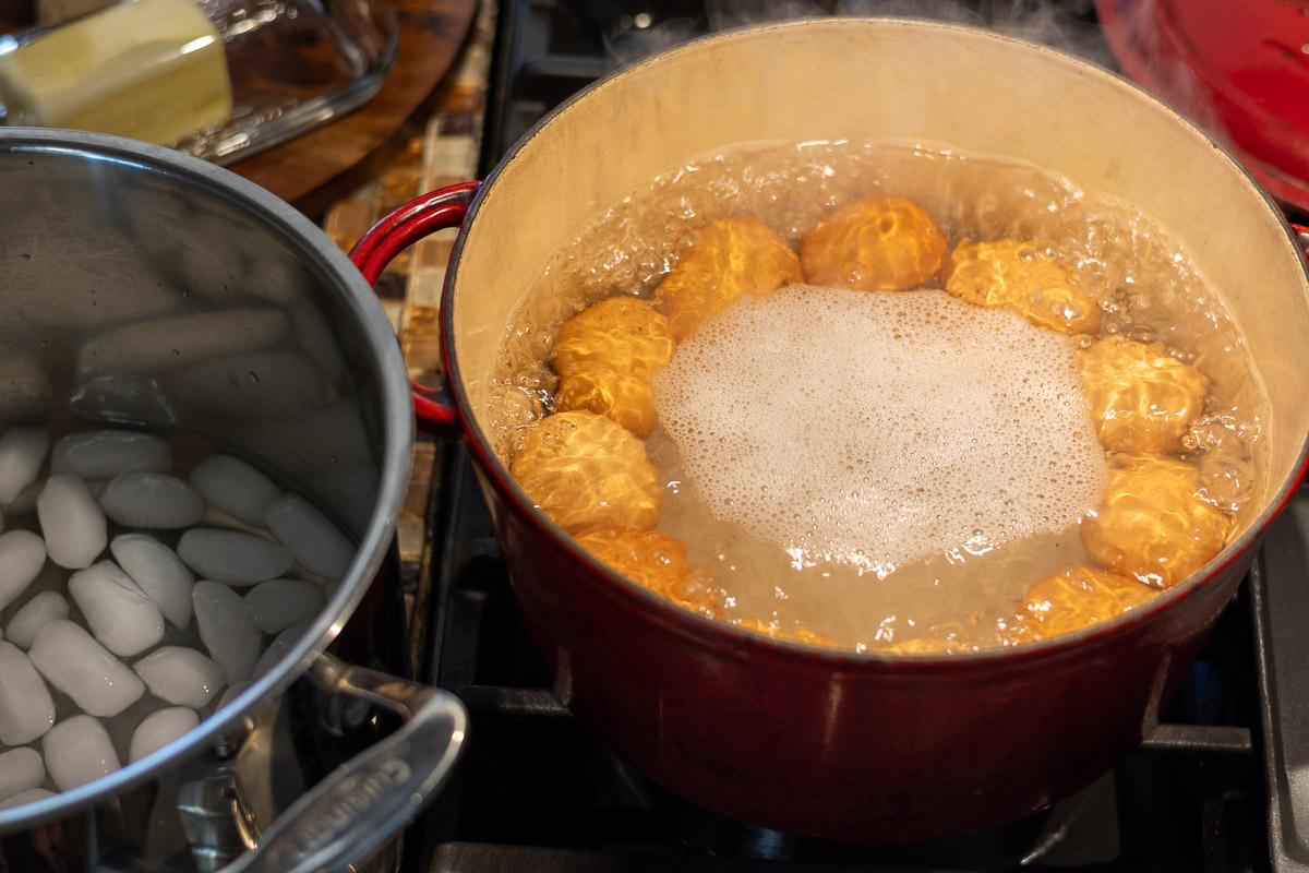 Eggs being hard boiled next to a pot of ice water.