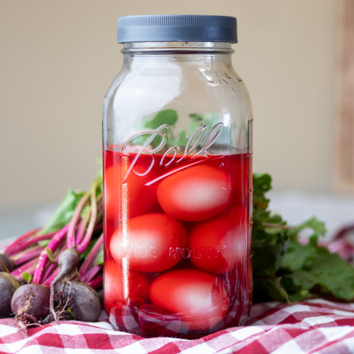Jar of pickled beets on top of gingham cloth and fresh beets.