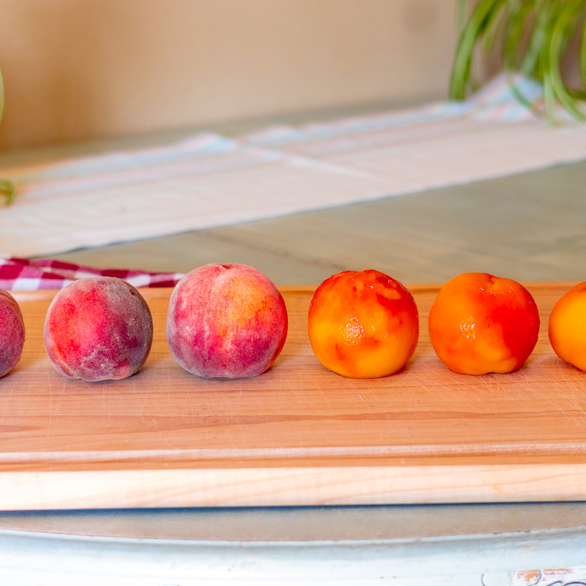 Three unpeeled peaches next to 3 peeled ones on a wooden cutting board.
