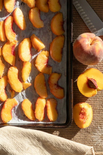 Frozen peaches on cookie tray alongside fresh peaches and a knife.