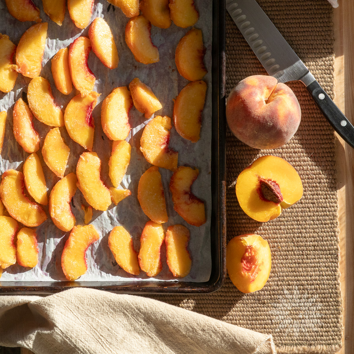 Frozen peaches on cookie tray alongside fresh peaches and a knife.
