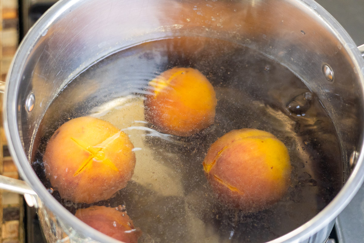 Four scored peaches in a pot of boiling water.
