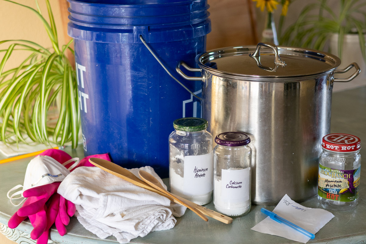 All the supplies needed to mordant cotton with aluminum acetate sitting on a table.