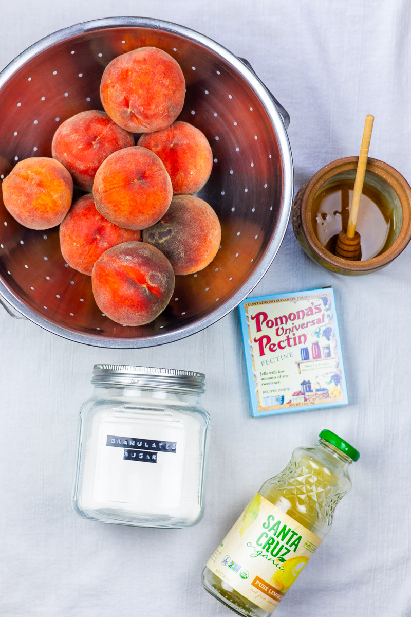 A flat lay of fresh peaches, honey, sugar, pomonas pectin and lemon juice.