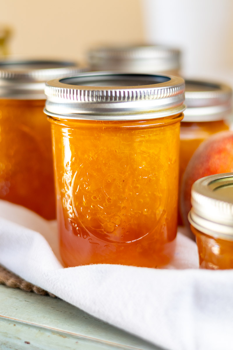 peach jam on table with white flour sack and fresh peach.