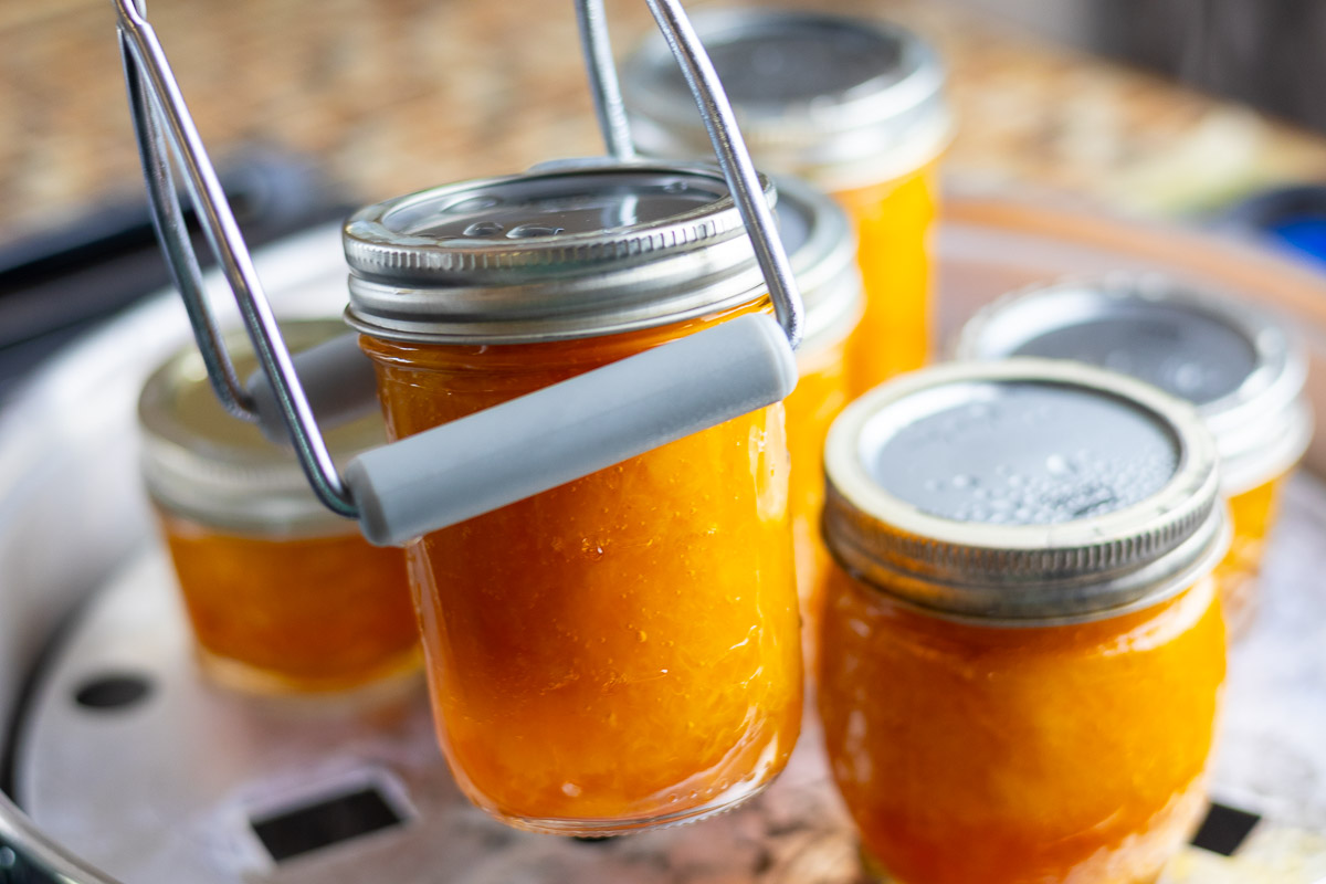 A jar lifter holding peach jam in front of steam canner.