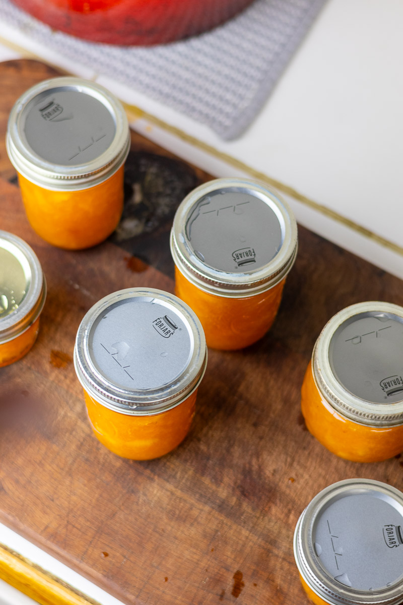 jars of peach jam with lids and rings on wooden cutting board.
