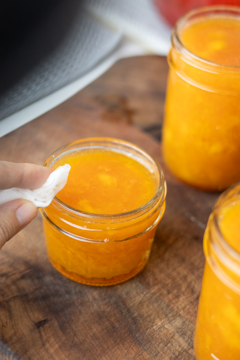 Wiping peach jam rims on jar.