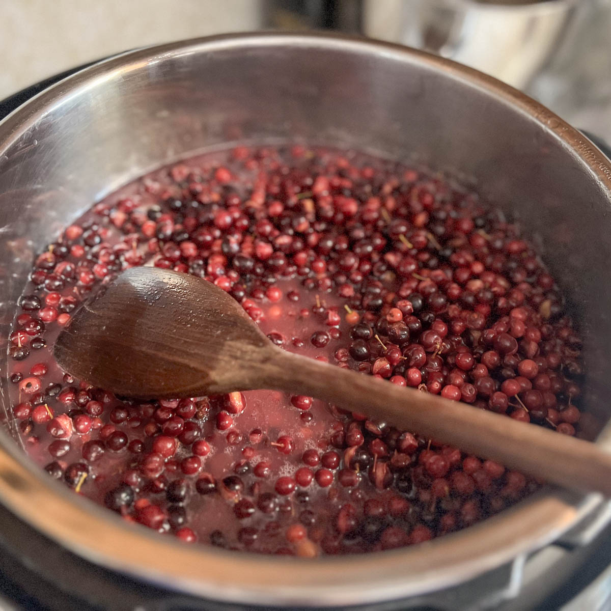 Chokecherries with water in pot and wooden spoon.