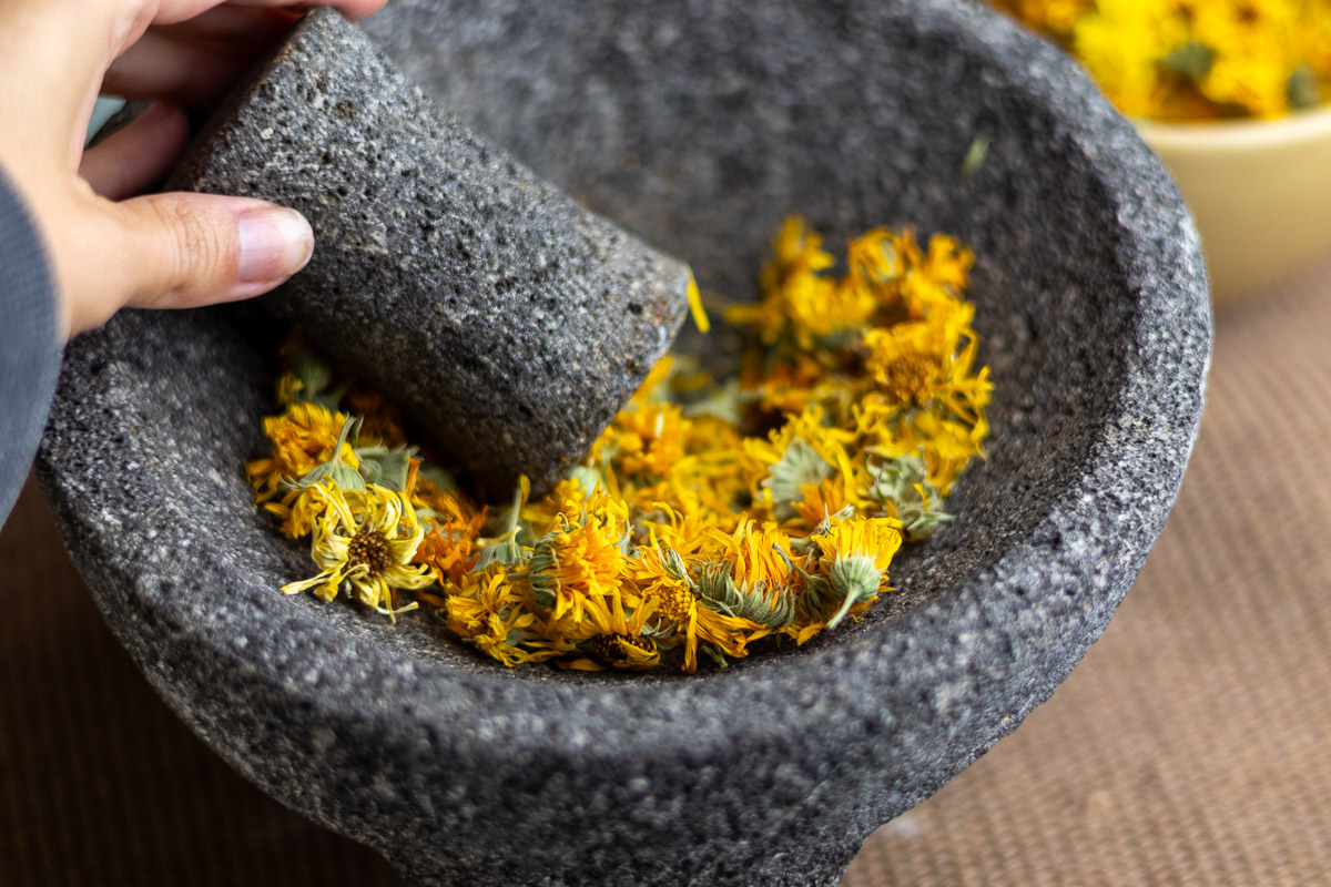 A grey mortar and pestle filled with whole calendula flowers.