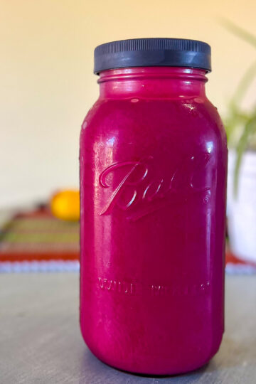 A half gallon mason jar on a blue table filled with fresh chokecherry juice.