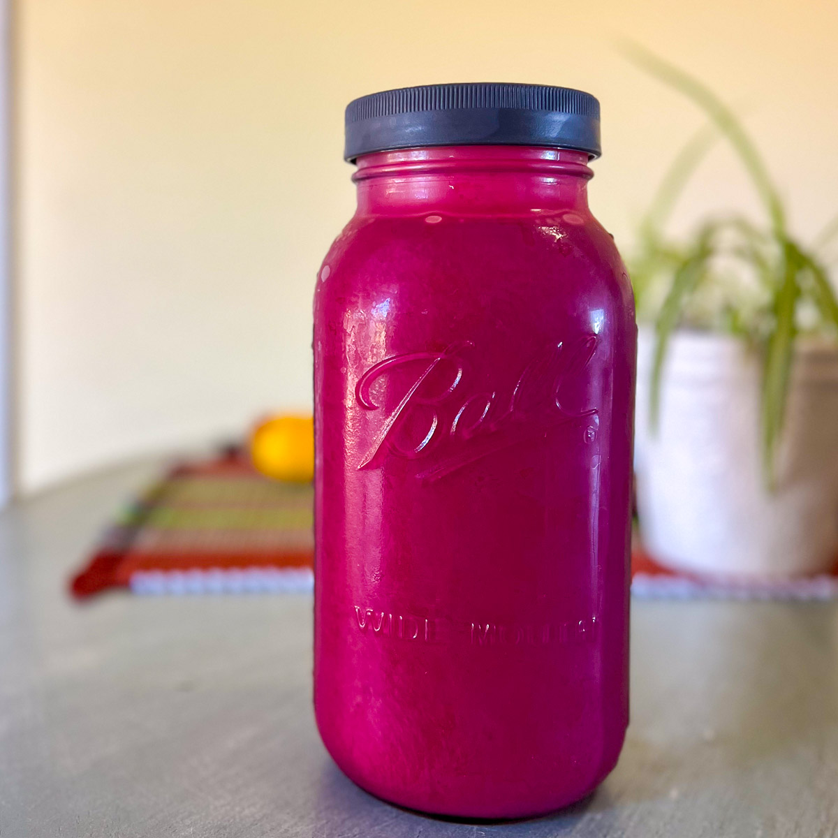 A half gallon mason jar on a blue table filled with fresh chokecherry juice.