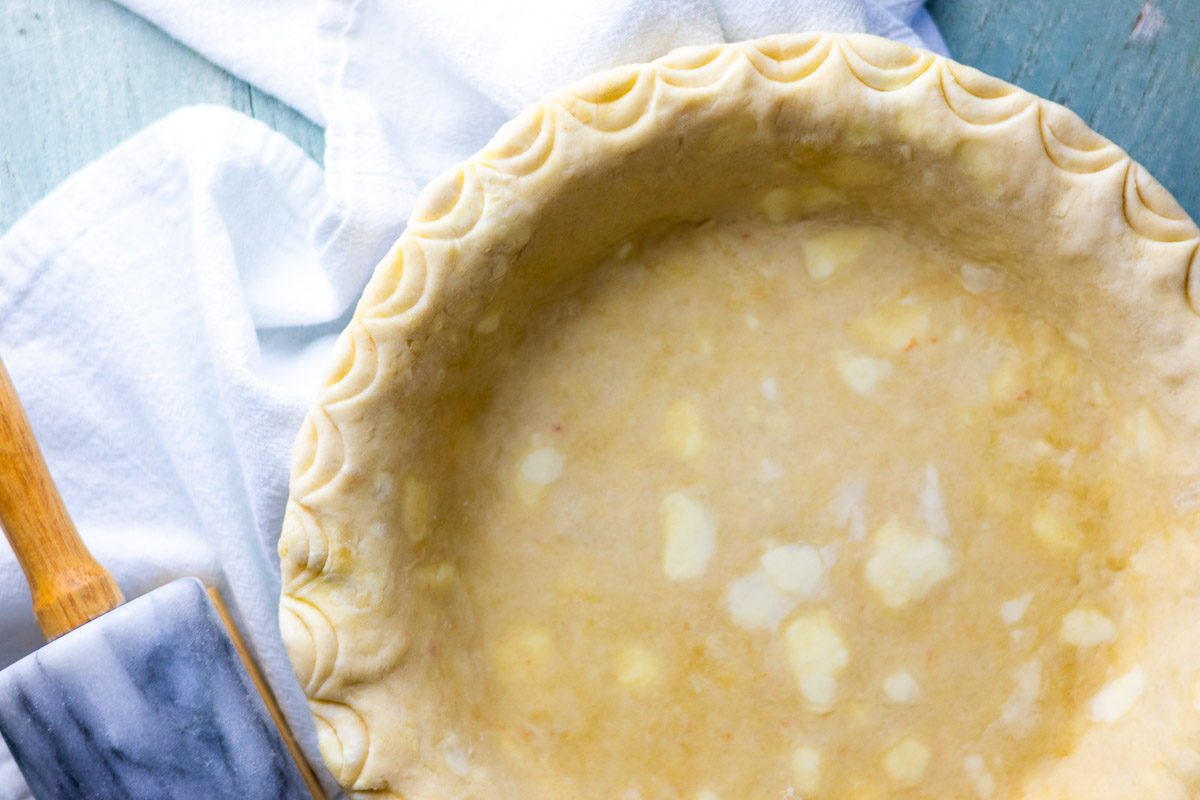 Flat lay of lard pie crust with scalloped edges and rolling pin.