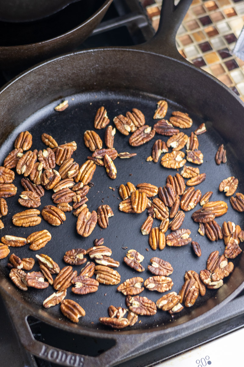 Whole pecans toasting on a cast iron skillet.