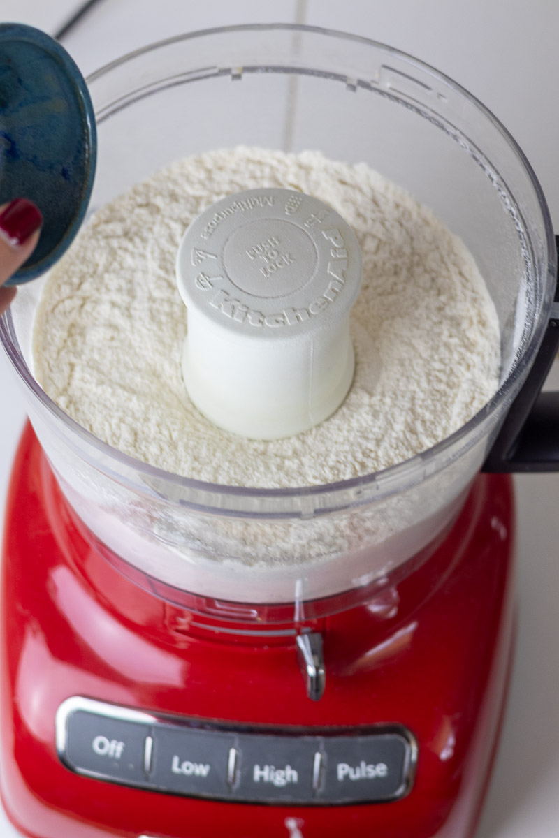 Adding salt and sugar to pie crust ingredients in red food processor.