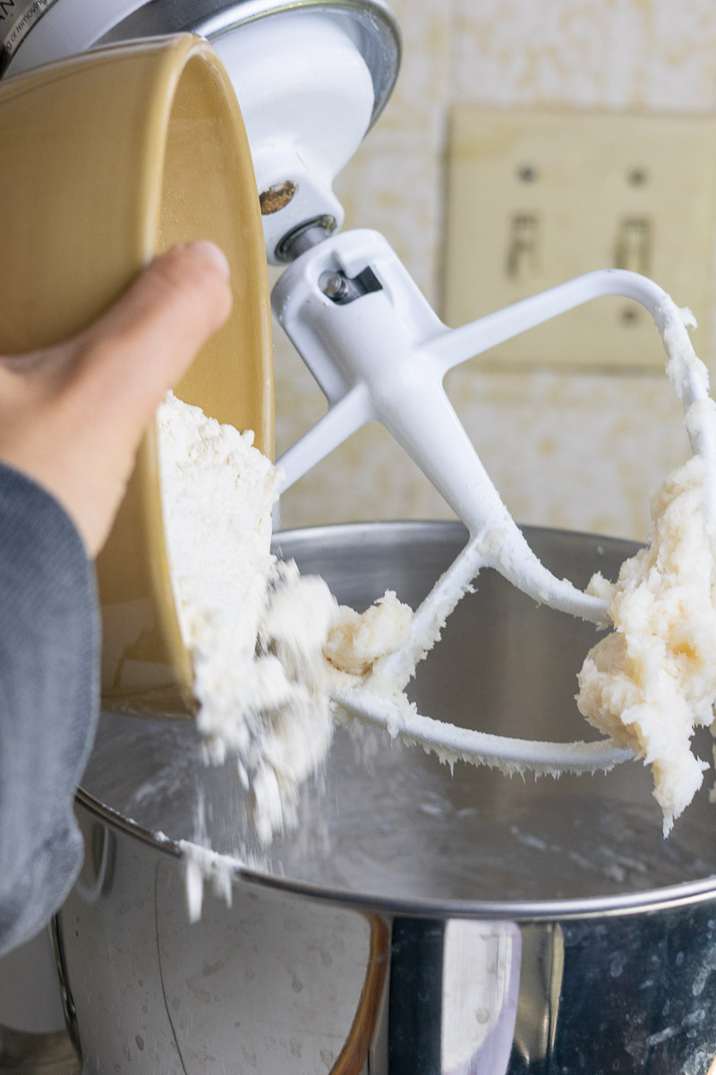 All purpose flour being poured into a stand mixer from a bowl.