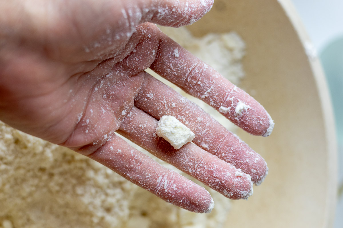 A hand showing an almond sized butter chunk in pie crust dough.