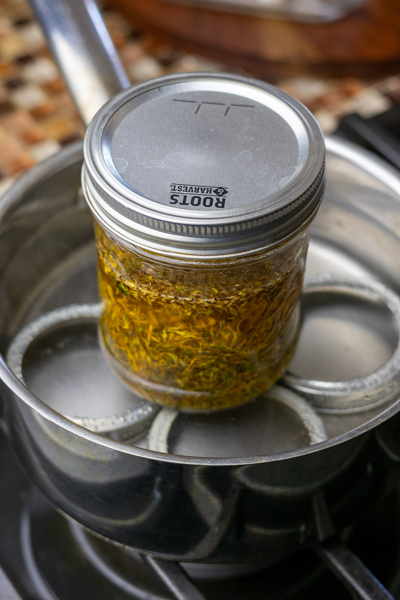 A jar of calendula oil and flowers being infused in a stovetop double boiler.