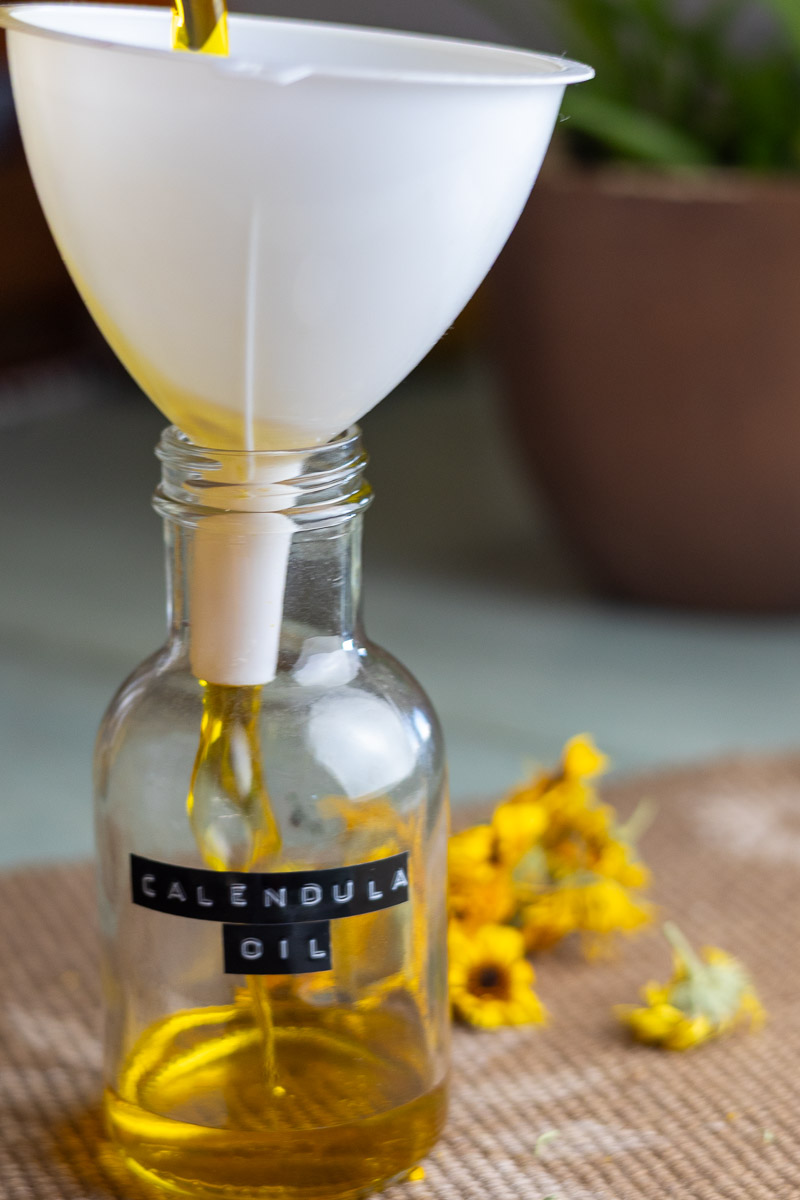 Pouring finished calendula oil in a pretty jar.