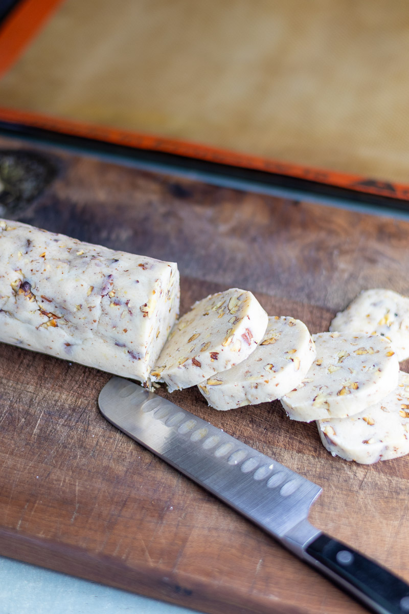 A log of pecan maple sandies being cut into coins.