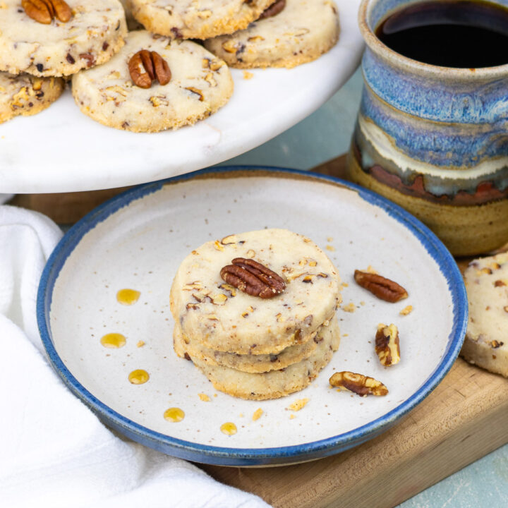 Three maple pecan sandies arranged on a plate, next to a full cup of coffee.