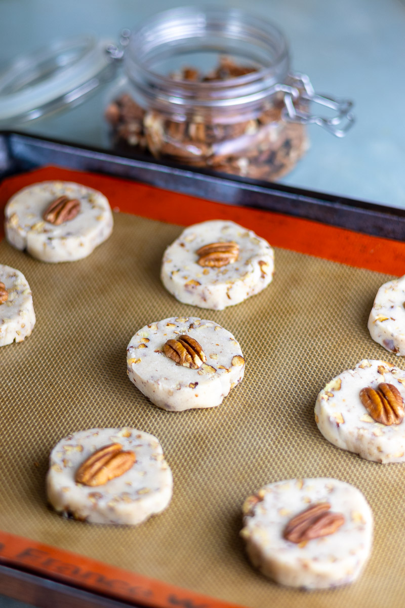 Maple pecan lard sandies ready to be baked next to a container of whole pecans.