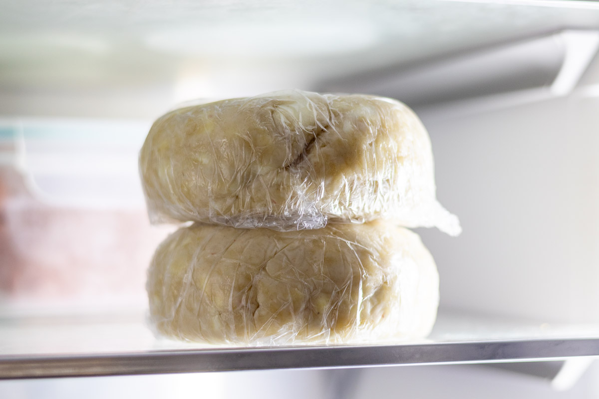 Two lard and butter pie crust dough disks wrapped in plastic in the refrigerator.