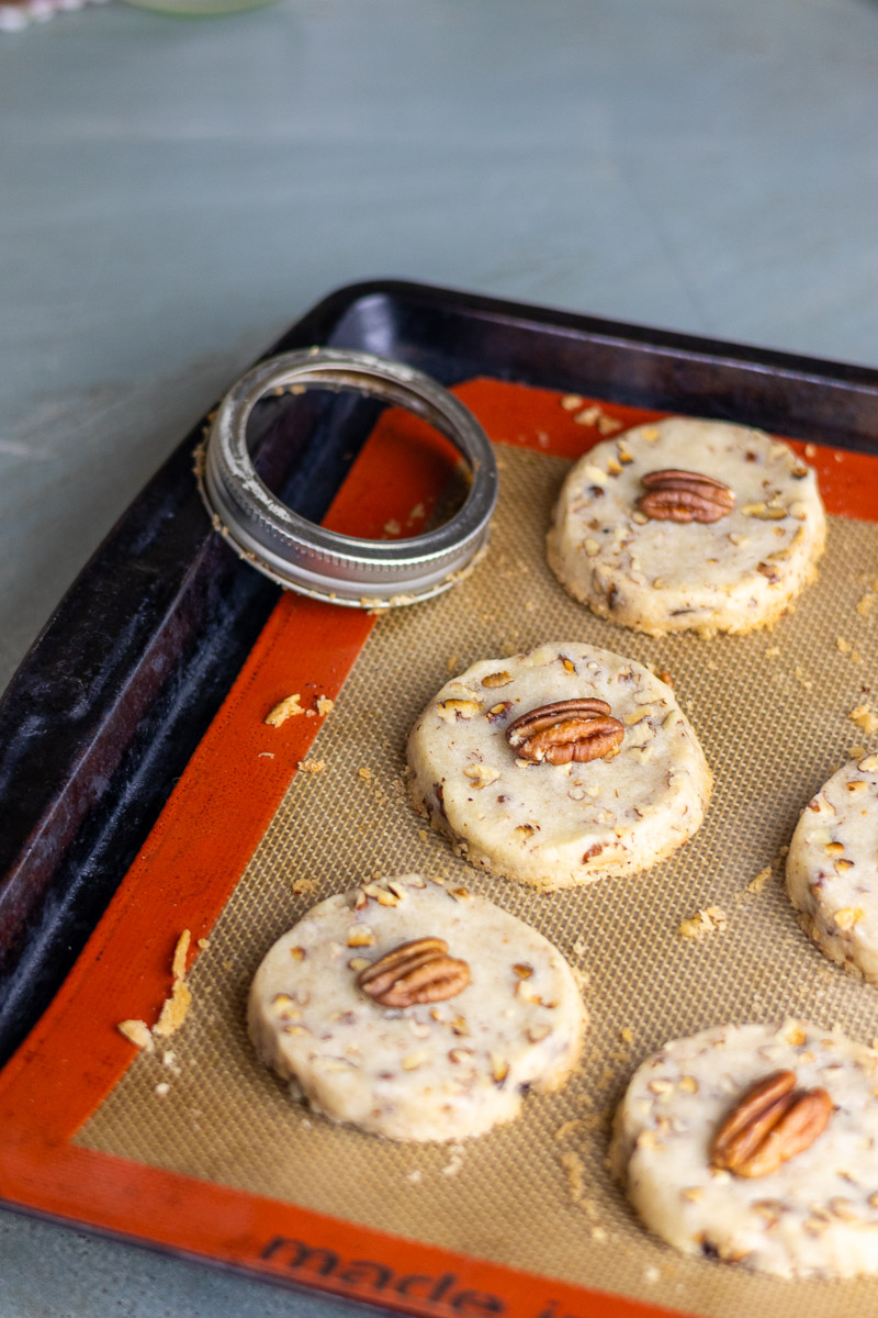 Maple pecan sandies cooling on a tray with a canning ring next to it.
