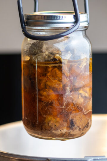A jar of pressure canned venison being held with jar lifter.