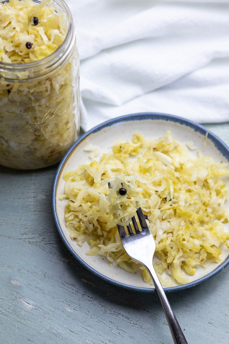 A plate and fork with juniper caraway kraut next to a jar filled with the kraut.