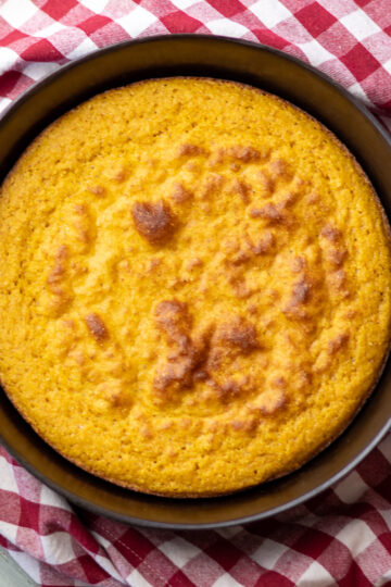 A cast iron skillet with gluten free cornbread on top of a red gingham cloth.