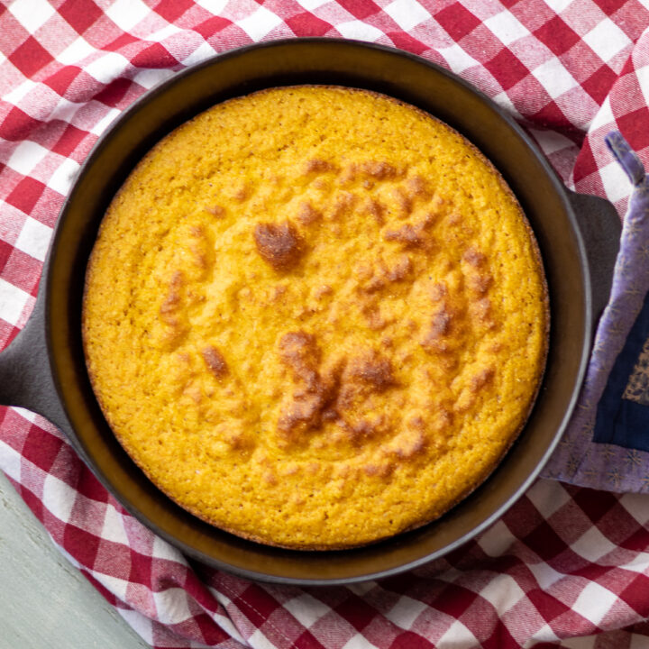 A cast iron skillet with gluten free cornbread on top of a red gingham cloth.