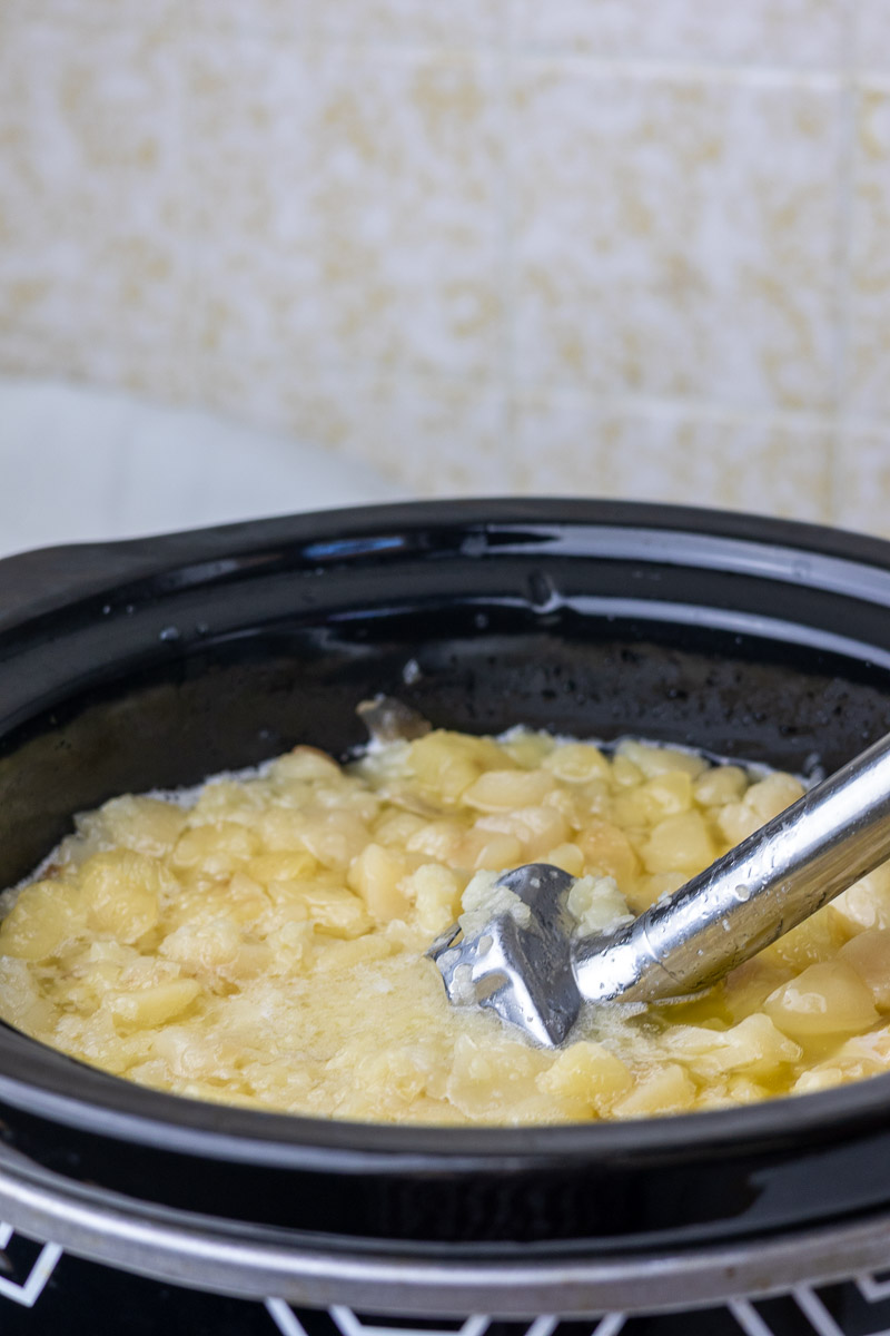 An immersion blender in a pot of cooking suet chunks.