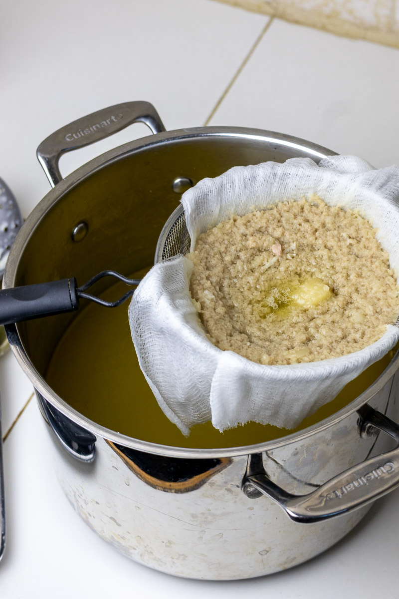A stainless steel pot full of strained fat and water separated from a mesh strainer of solids.