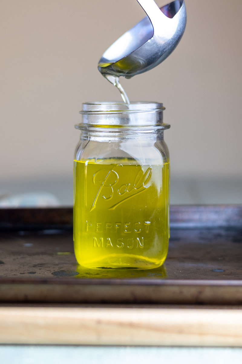 A silver ladle pouring hot tallow in a ball mason jar.