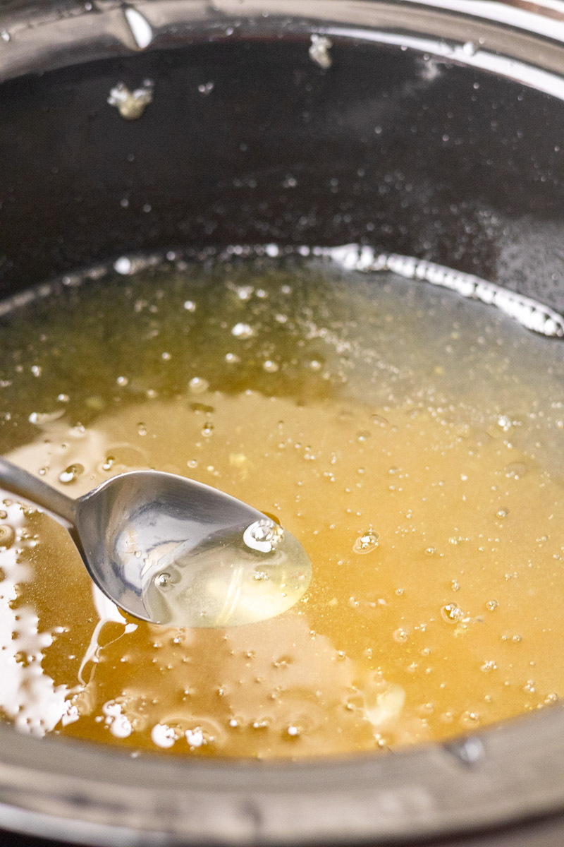 a spoon halfway in a crockpot of dry rendered tallow.